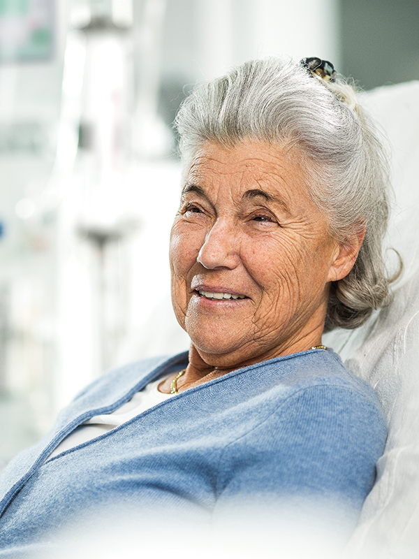 Eldery woman smiles and sitting in a bed with a raised backrest